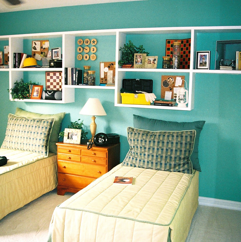 A bedroom with two beds and shelves on the wall.